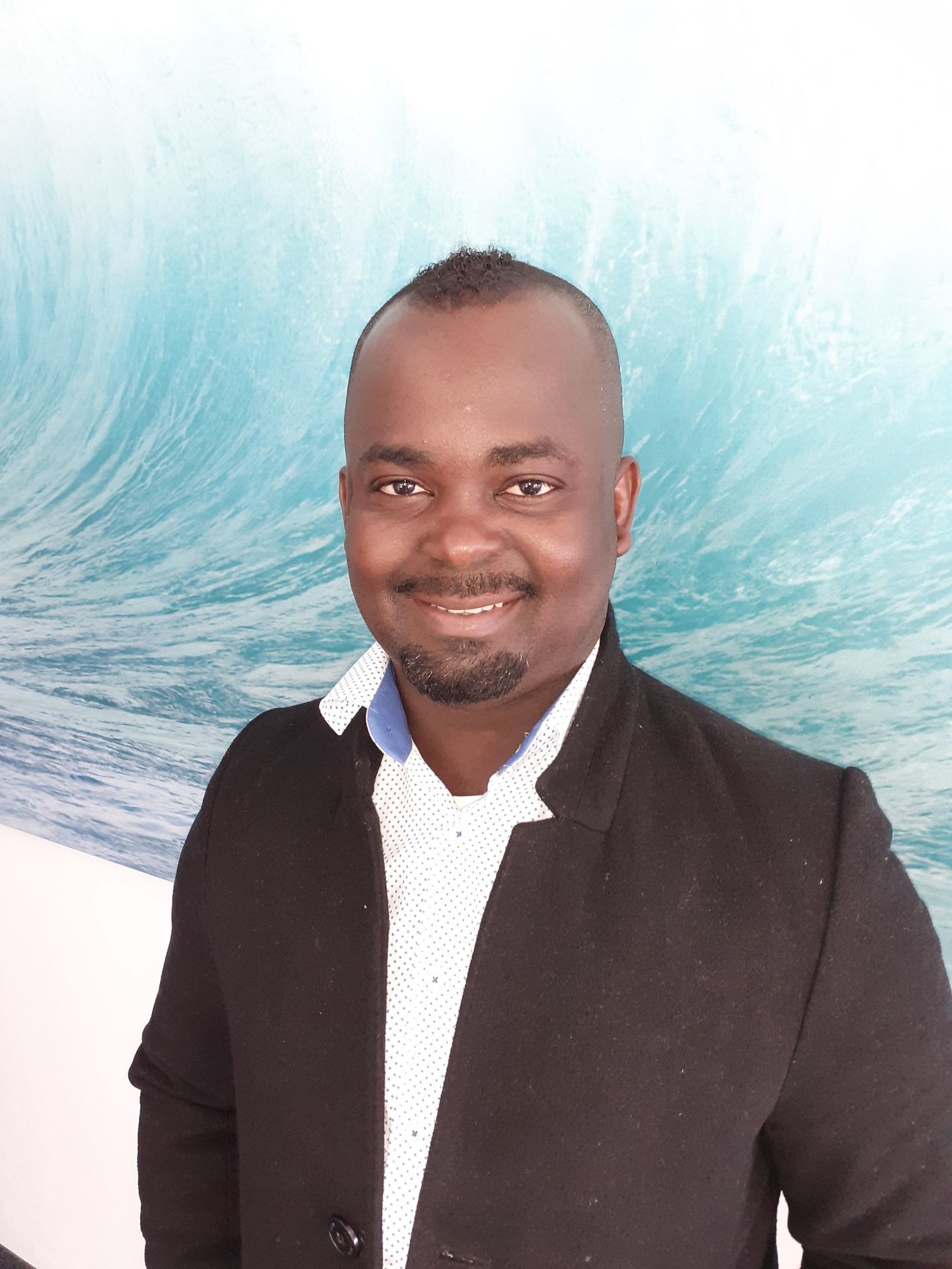 Person in a black blazer and white shirt standing in front of a wall with a wave mural.