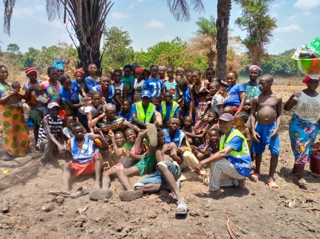 Large group of people, including children and adults, smiling and posing together outdoors under palm trees.